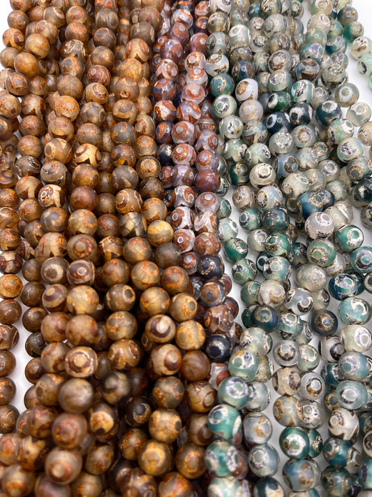 The 8mm Tibetan Agate Round IT strands feature multicolored beads arranged closely together, showcasing earthy tones such as browns, greens, and grays, with diverse natural patterns and textures.