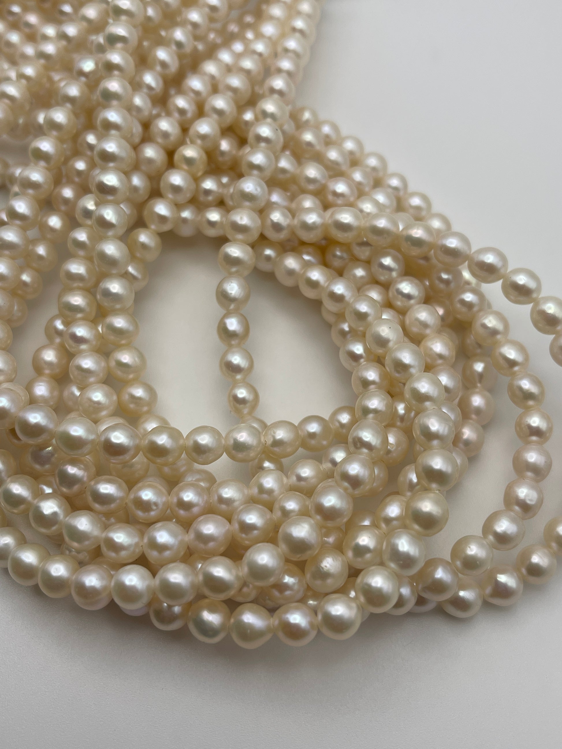 A close-up view of several strands of 5.5-6mm white potato pearls, with the pearls appearing smooth and slightly shiny under the light. The strands are loosely coiled and displayed against a plain, light-colored background.