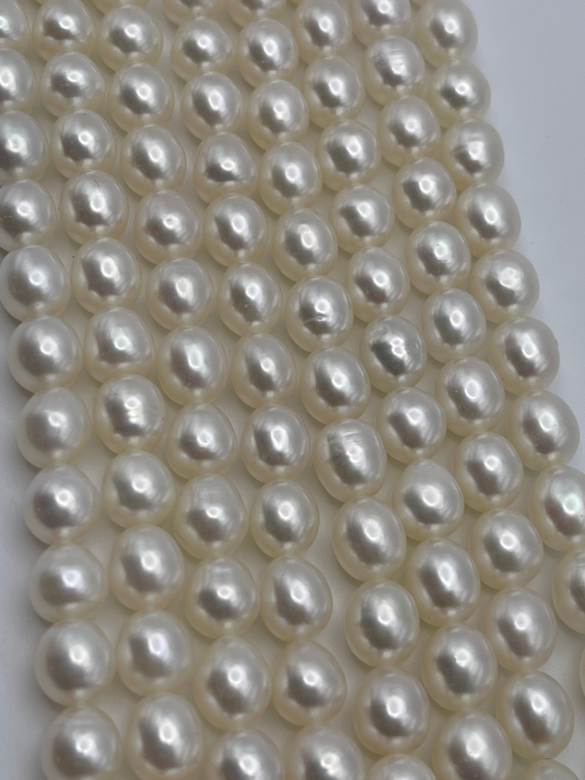 A close-up view of multiple rows of 7.5-8mm white rice pearls reveals their uniformly round shape and smooth, glossy surface. The pearls are meticulously arranged, creating a patterned, textured appearance that showcases their shimmering beauty.