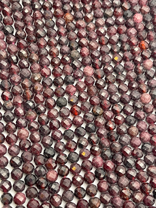 The 5mm Fac Garnet Rnd beads, in various shades of burgundy, red, and dark purple, are tightly lined up next to each other, filling the entire frame. Their polished surfaces create a shimmering, repetitive pattern.