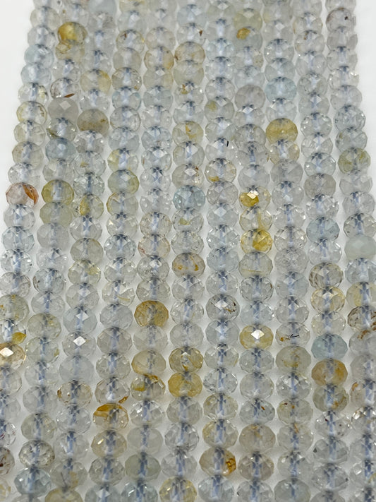 Strings of 5mm Fac Topaz Rondell beads in an array of light gray and yellow hues are strung closely together. The beads have a translucent quality with some displaying flecks of brown and other colors, creating a shimmering effect under the light.