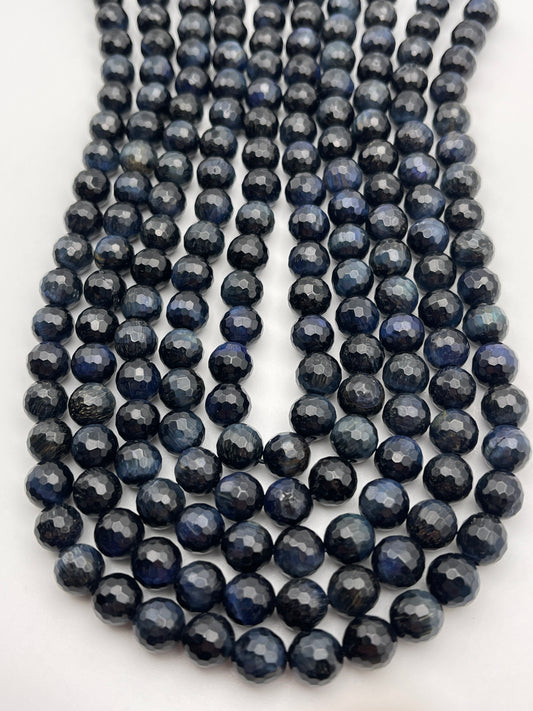 Rows of polished 8mm Round Faceted Blue Tiger's Eye beads are arranged closely together. Each bead is faceted, giving it a shiny, reflective surface. The beads appear to be made of gemstone, creating a pattern of shimmering light and dark tones.
