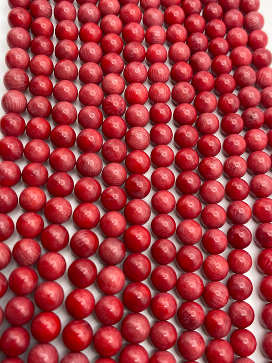Rows of 8mm Coral beads, small and spherical in shape, are closely aligned on a light background, creating a visually striking pattern. The coral beads have a slight shine and varied tones of red, adding texture and depth to the image.