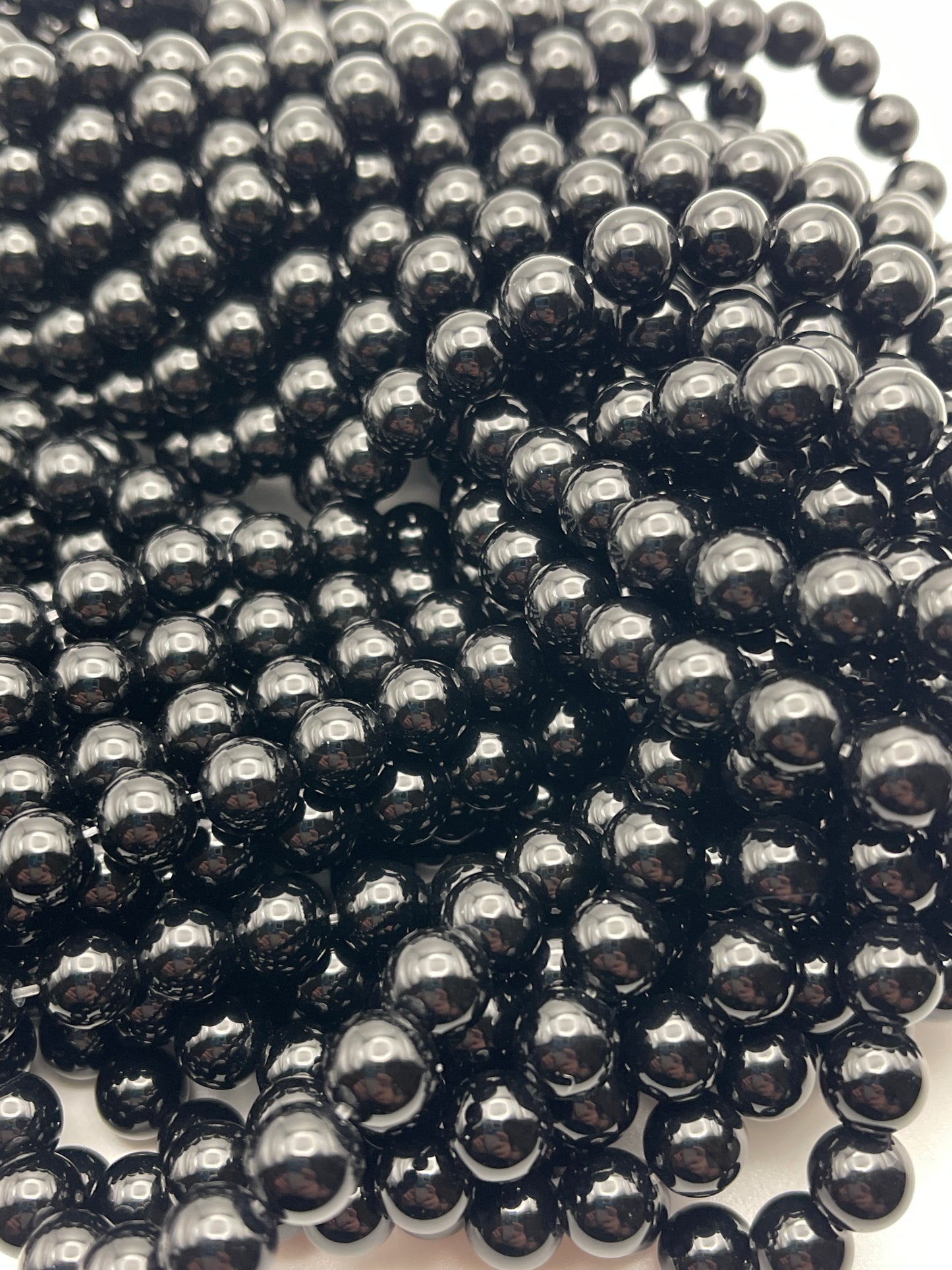A close-up shot of numerous 8mm Black Onyx beads, tightly clustered together. The beads are uniform in size and have a glossy, reflective surface, creating an intricate and visually striking pattern.