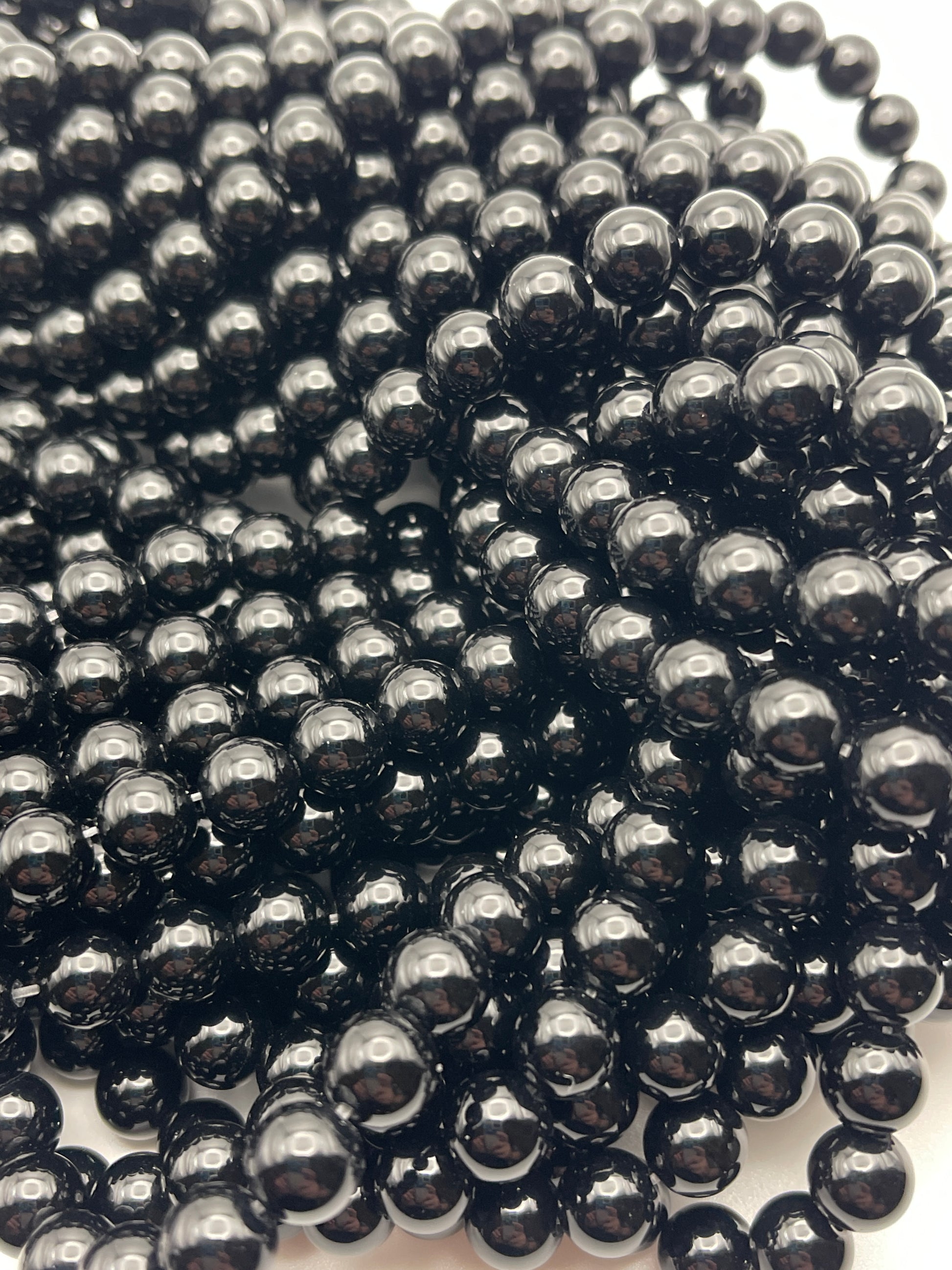 A close-up shot of numerous 8mm Black Onyx beads, tightly clustered together. The beads are uniform in size and have a glossy, reflective surface, creating an intricate and visually striking pattern.