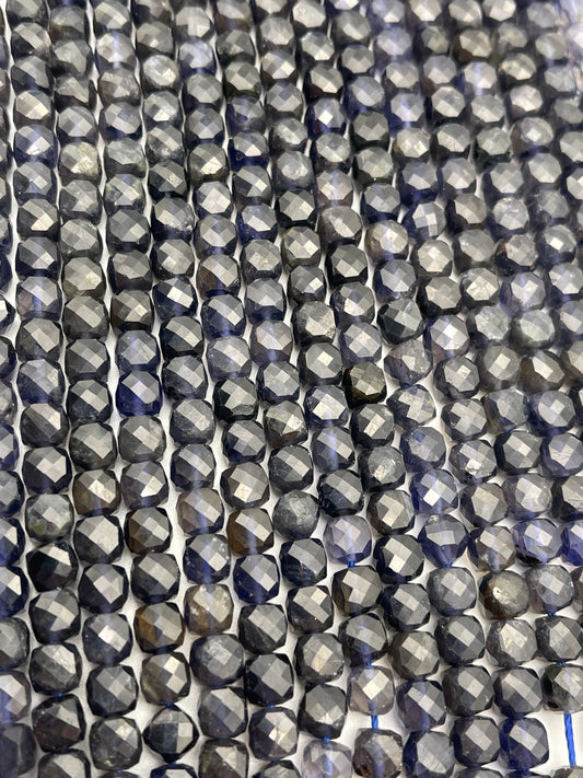 Close-up image showcasing multiple rows of 7mm Square Faceted Iolite beads with a greyish-blue hue, creating a sparkling effect under the light. The beads are uniformly arranged, emphasizing their symmetrical cuts and reflective surfaces.