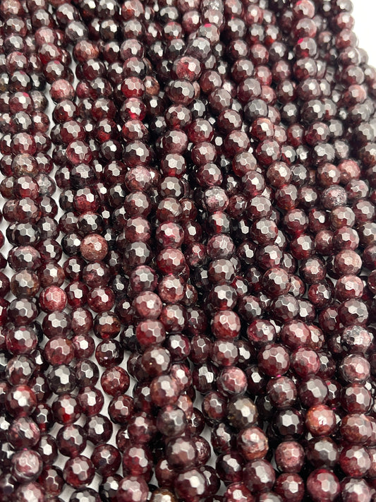 A close-up image of multiple strands of 7mm faceted garnet beads. The beads exhibit a rich, deep red hue and a polished, sparkling surface. The strands are intricately arranged, filling the entire frame.